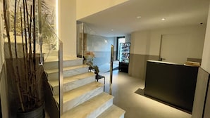 Een modern interieur met een marmeren trap, een receptiebalie en een automaat.