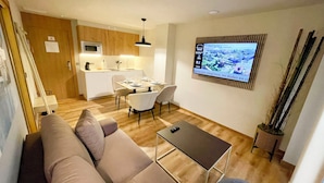 Een ruimtelijk ingerichte leefruimte met een kitchenette, eethoek en een aan de muur bevestigde flatscreen-tv.