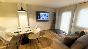Een moderne woonkamer met een eethoek, een flatscreen televisie aan de muur, een bank en een bijzettafeltje.