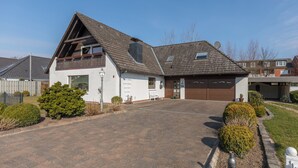 Ein zweistöckiges Haus mit geneigtem Dach, einer Garage und einem gepflasterten Auffahrtsweg.