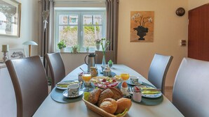 Ein Esstisch, gedeckt für ein Frühstück mit verschiedenen Gerichten, einer Kaffeekanne und einem Fenster mit Vorhängen.