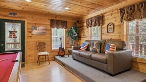 A cozy room with a pool table, a leather couch with American flag pillows, a guitar, and a wooden ceiling. - KunTree Cabin by Beyond Expectations: 3BR Cabin w/ Hot Tub, Sauna & Pool Table (Sevierville)
