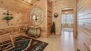 A wooden interior with a circular mirror, a dresser, a patterned rug, and a small Christmas tree. - KunTree Cabin by Beyond Expectations: 3BR Cabin w/ Hot Tub, Sauna & Pool Table (Sevierville)