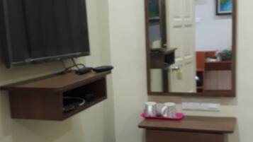 A small room with a television on a shelf, a mirror, a small table, and a trash bin.