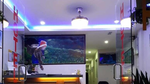 Zona de recepción de hotel con un tapete que dice 'BIENVENIDOS', un mostrador de recepción y un cuadro grande de una persona en un bosque.