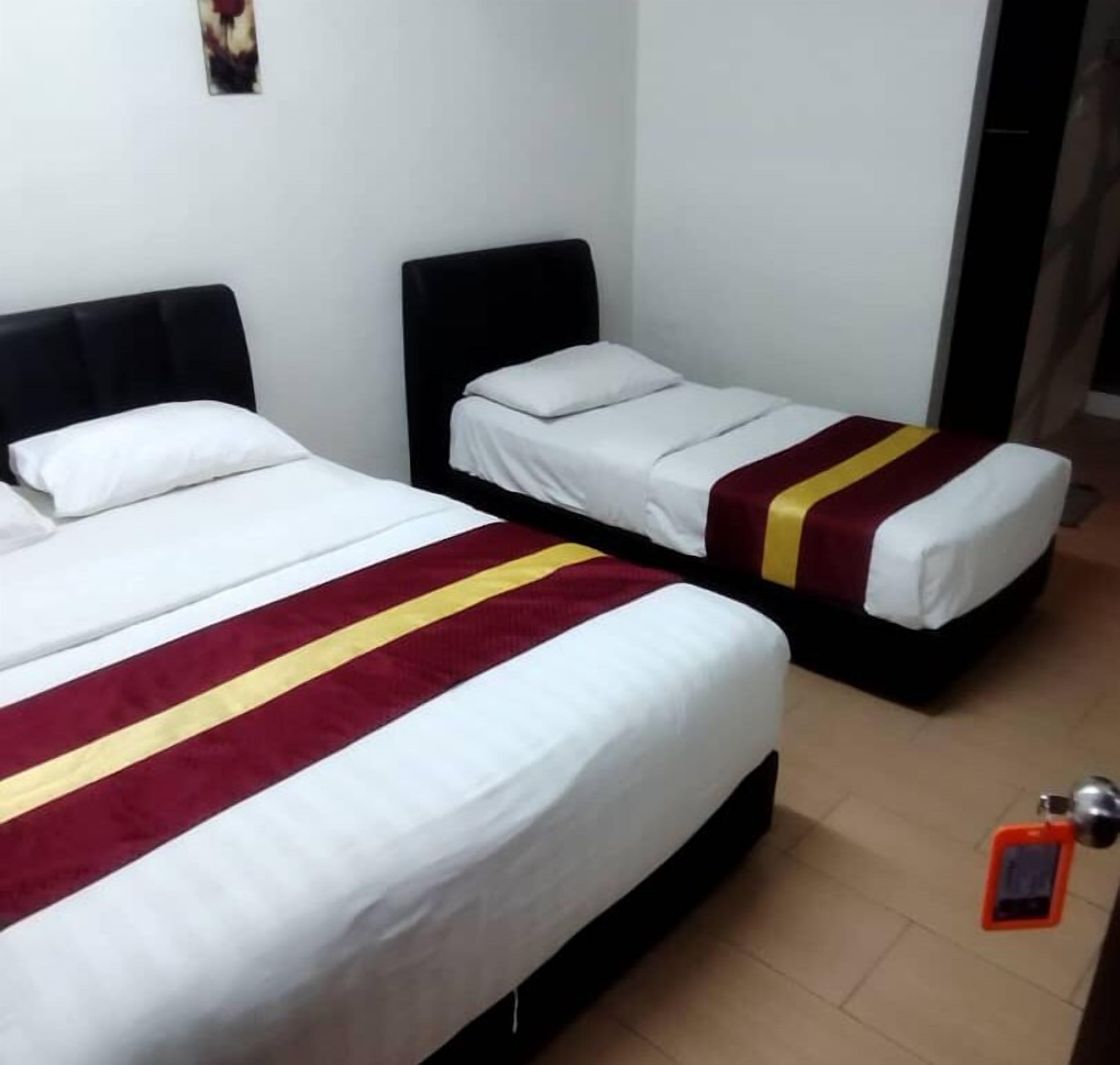 Two single beds with white linens and red and yellow striped bedspreads in a room with plain walls and a tiled floor.
