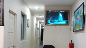 Un pasillo de hotel con una recepción, una silla de oficina negra, una consola de madera con un jarrón de flores y un cuadro en la pared.