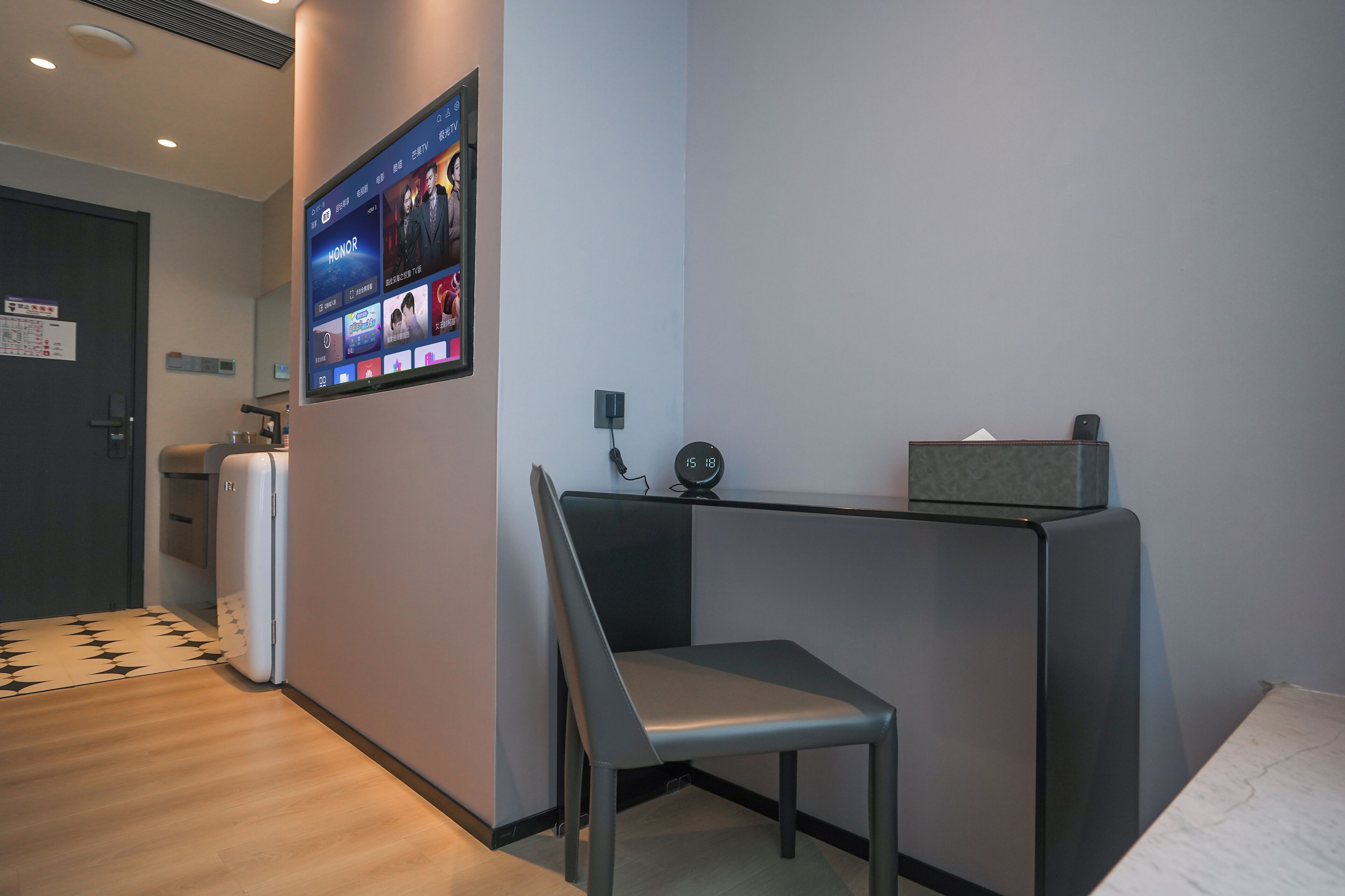 A hotel room with a desk, chair, and a flat-screen TV mounted on the wall displaying a movie.