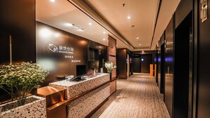 Un área de recepción moderna de hotel, con un mostrador de recepción, una pantalla digital y una planta en maceta.