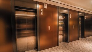 Un pasillo con tres puertas de ascensor, cada una con acabado metálico y un panel de control en la pared.
