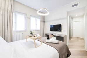 Habitación de hotel moderna con cama, mesita de noche, televisor y vista al pasillo.
