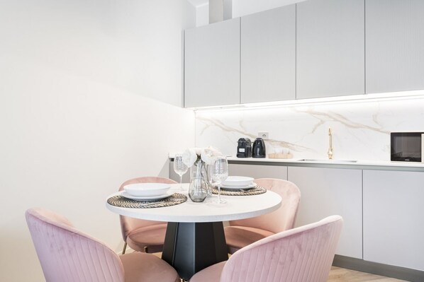 A modern kitchen with a round dining table, two chairs, and a countertop with a coffee machine.