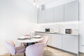 Una cocina moderna con armarios blancos, encimera de mármol y una mesa redonda con sillas rosadas.