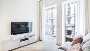 A modern living room with a flat-screen TV, a sofa, a coffee table, and a window with a view of buildings. - Easylife - Duomo Deluxe Apartments #1 (Milano)