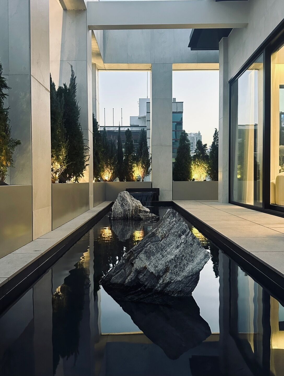 Ein moderner Innenpool mit einem großen Felsen im Zentrum, umgeben von Betonwänden und Glasfenstern.