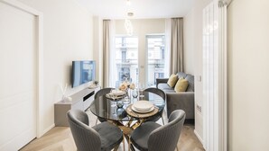 Un salon moderne avec une table à manger en verre, des canapés gris et un téléviseur à écran plat.