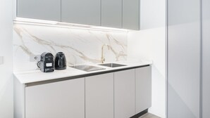 A modern kitchen with a marble backsplash, two black coffee makers, and a stainless steel sink. - Easylife - Duomo Deluxe Apartments #5 (Milano)