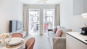 A modern living room with a sofa, dining table, and chairs. There is a television on a stand, and a large window with curtains. - Easylife - Duomo Deluxe Apartments #5 (Milano)