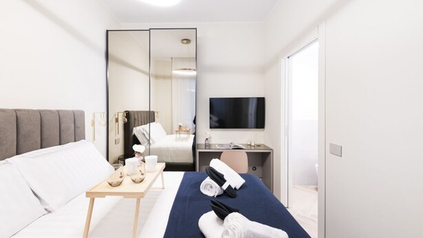 Une chambre d’hôtel avec un lit, un bureau, une télévision, un miroir et une porte.