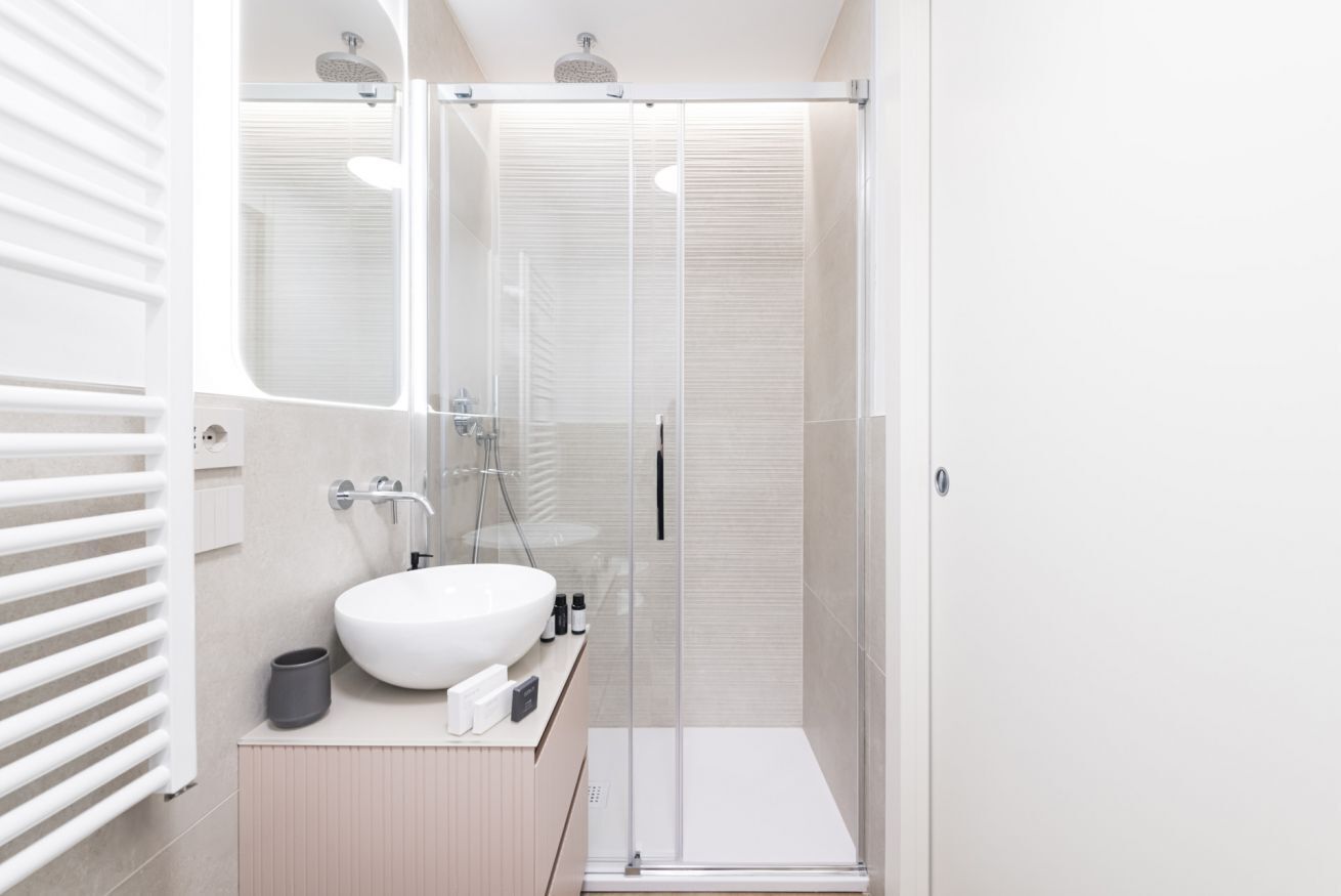 A modern bathroom with a glass shower enclosure, a white sink, and a beige vanity.