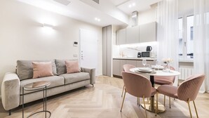 Un salon moderne avec un canapé, une table ronde et des chaises, une cuisine équipée et une fenêtre avec des rideaux.