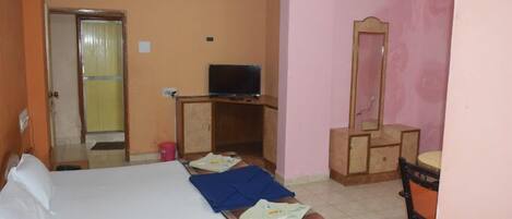 Una habitación de hotel con una cama, televisión, cómoda y espejo.