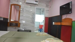 Habitación de hotel con cama, televisión, espejo y baño visible a través de una puerta abierta.