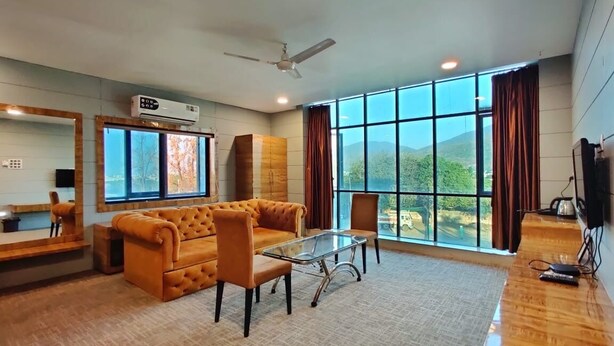 Un salón amplio con un ventanal grande, un sofá, una mesa de centro de cristal y un escritorio de madera.
