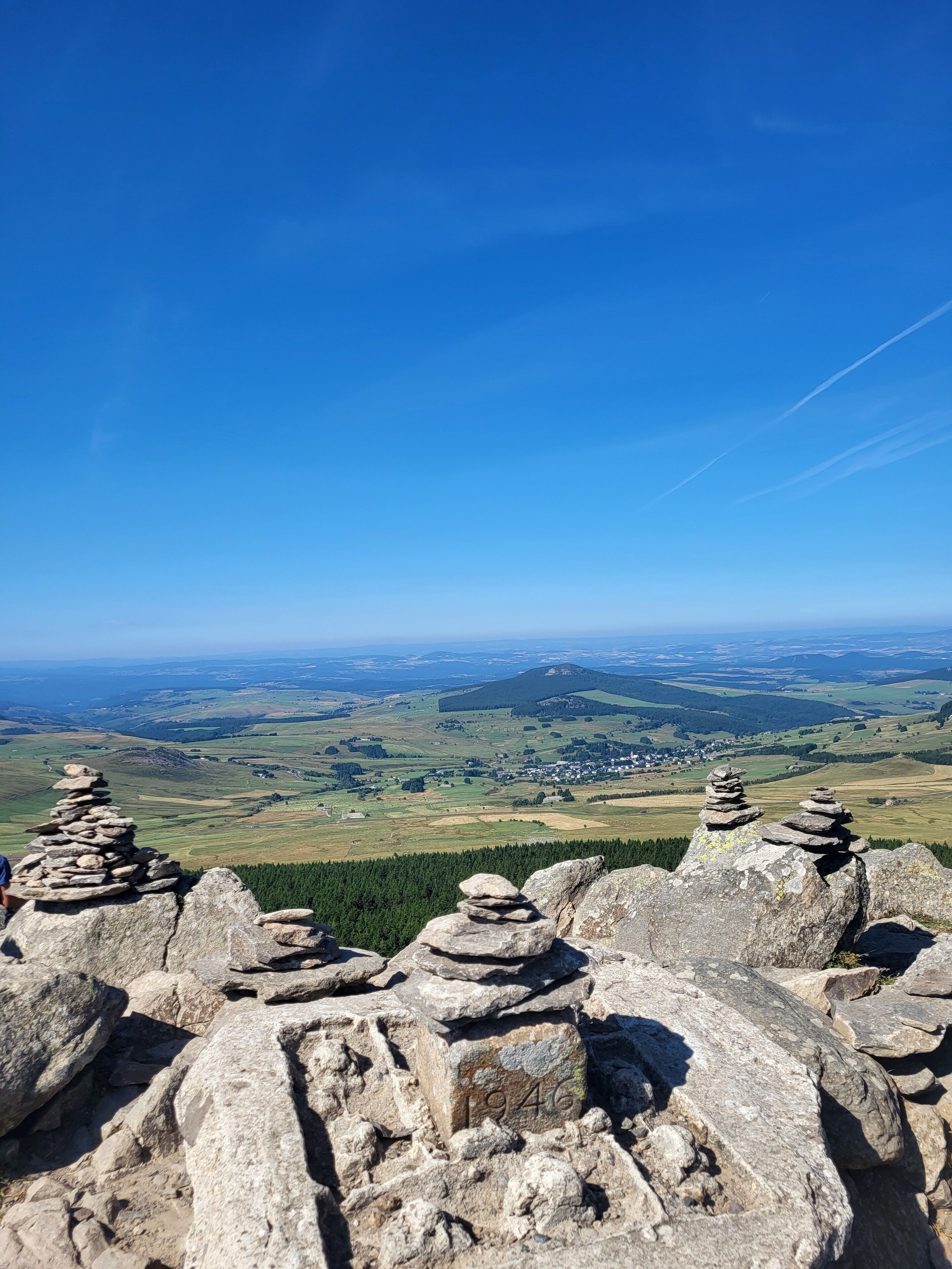 Ein weitreichender Panoramablick auf eine Berglandschaft, im Vordergrund Steinmalsteine und in der Ferne ein Dorf.
