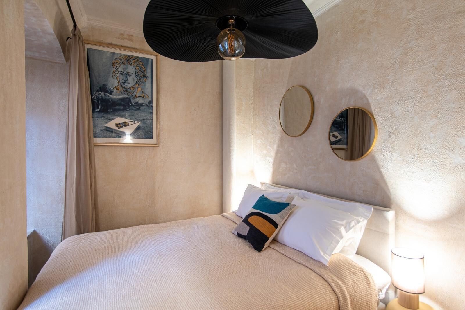 A hotel room with a bed, a ceiling fan, a painting, and two wall mirrors.