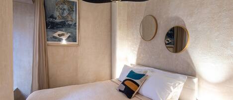 A hotel room with a bed, a ceiling fan, a painting, and two wall mirrors.