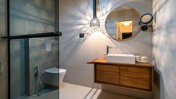 Un baño moderno con cabina de ducha de vidrio, tocador de madera con lavamanos y un espejo grande.