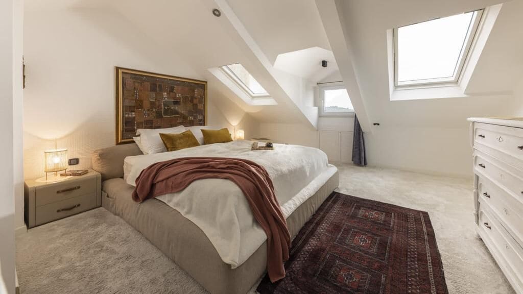 Een slaapkamer met een bed, nachtkastjes, een dressoir, een vloerkleed en dakramen.