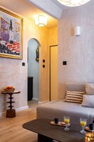 Uma sala de estar aconchegante com um sofá, uma mesa de centro com bebidas, uma fruteira e um quadro na parede.