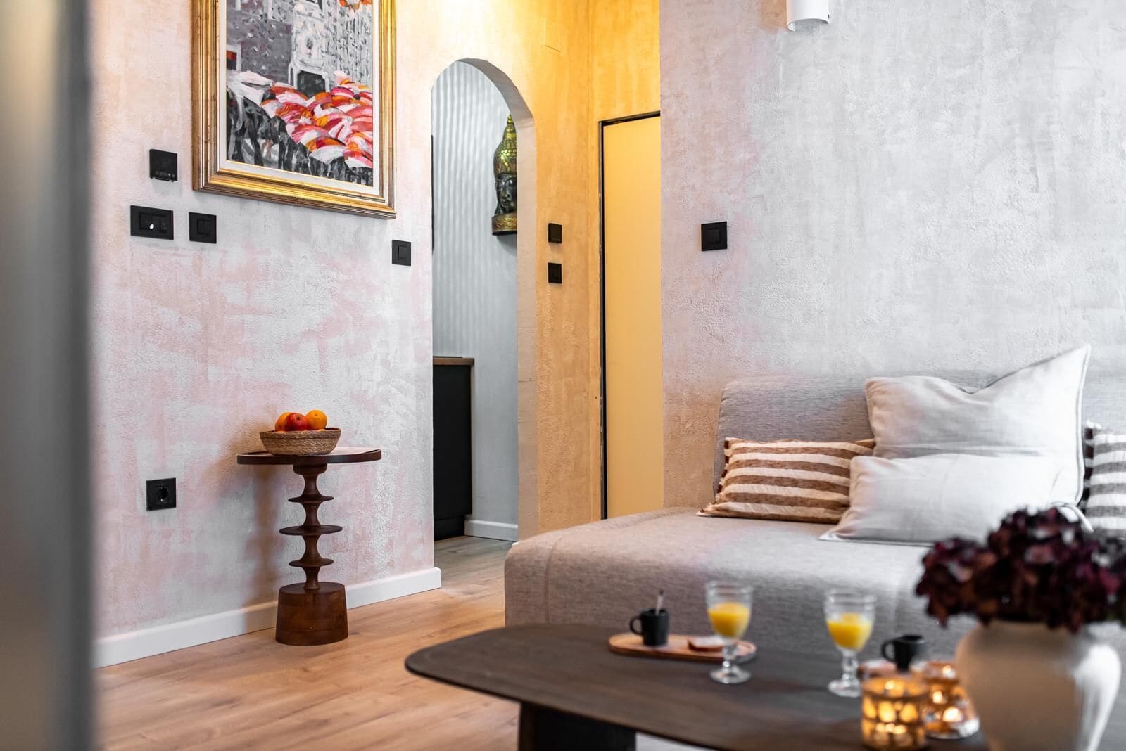 Una habitación de hotel moderna con una cama, una pequeña mesa con fruta, una mesita de centro con bebidas y un cuadro en la pared.