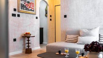 Una habitación de hotel moderna con una cama, una pequeña mesa con fruta, una mesita de centro con bebidas y un cuadro en la pared.