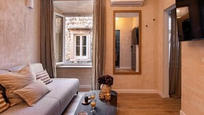 Une chambre d’hôtel moderne, dotée d’un canapé, d’une table basse avec des boissons, d’une télévision et offrant une vue sur une cour intérieure par une fenêtre.