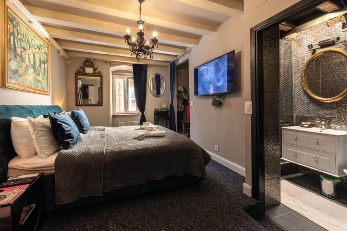 Un dormitorio con una cama grande, televisor, candelabro y un baño con un espejo redondo.