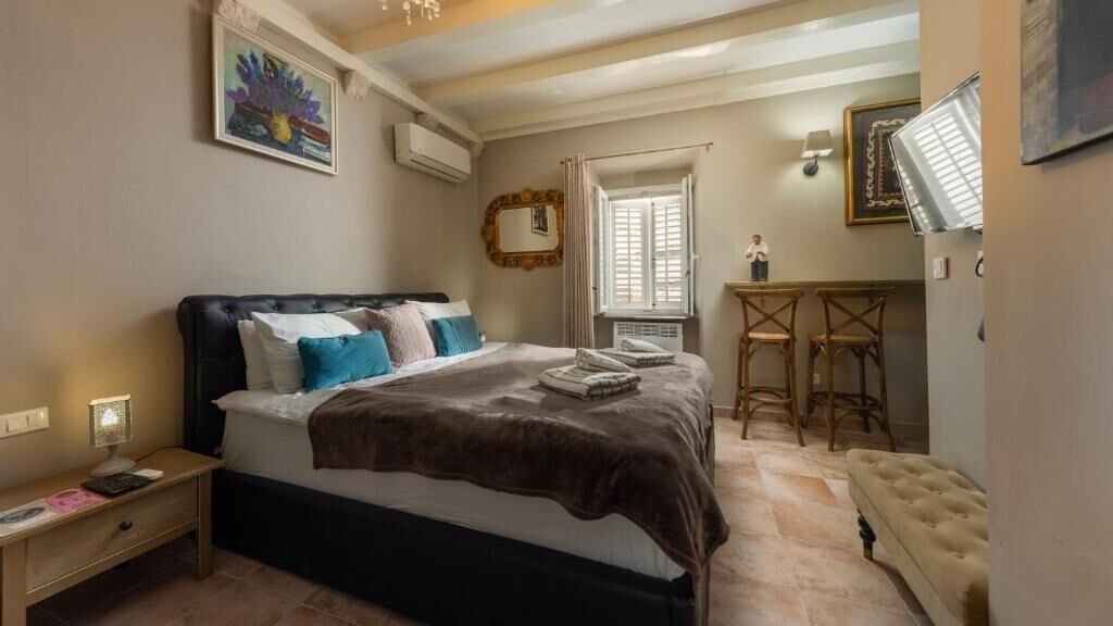 Un dormitorio con una cama grande, una mesita de noche, un escritorio con dos sillas y una ventana con contraventanas.