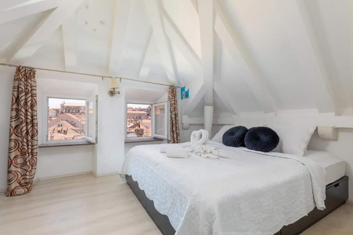 Un dormitorio con una cama grande, dos ventanas y vistas a edificios.