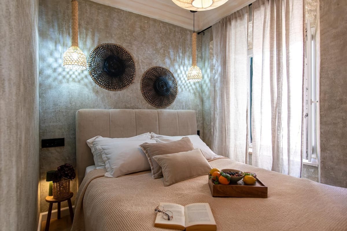 Un dormitorio con una cama grande, una mesita de noche con lámpara y una ventana con cortinas.