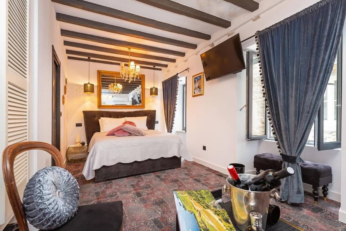 Un dormitorio con cama, televisor, candelabro y ventana con cortinas.