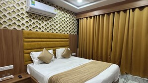 Une chambre d’hôtel comprenant un lit, une table de chevet, une télécommande, un climatiseur fixé au mur, un ventilateur de plafond et un papier peint à motifs.