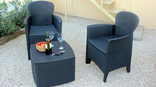 Two dark wicker chairs and a matching table with a basket and bottles.