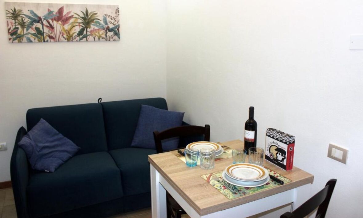 A small living area with a dark green sofa, a wooden dining table set with plates, glasses, and a bottle of wine.