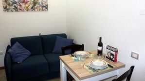 A small living area with a dark green sofa, a wooden dining table set with plates, glasses, and a bottle of wine.