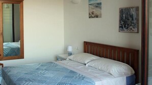 A bedroom with a bed, a nightstand, a mirror, and two wall-mounted pictures.