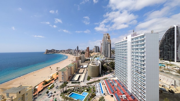 Un paisatge urbà costaner amb un hotel a primera línia de platja que disposa de múltiples pisos, una piscina i vistes a l'oceà.