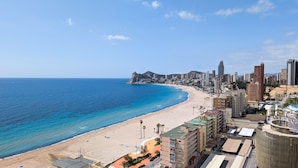 Paisatge urbà costaner amb una platja, edificis alts i un turó rocos on destaca.