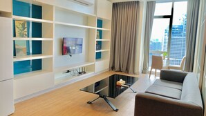 A modern living room with a flat-screen TV, built-in shelves, a glass coffee table, a sofa, and a view of a cityscape through large windows. - WELL-SHAPED Suites At PLATINUM KLCC (Kuala Lumpur)
